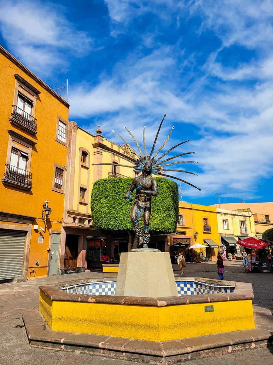 The Aztec Dancer statue in Queretaro against a blue sky.