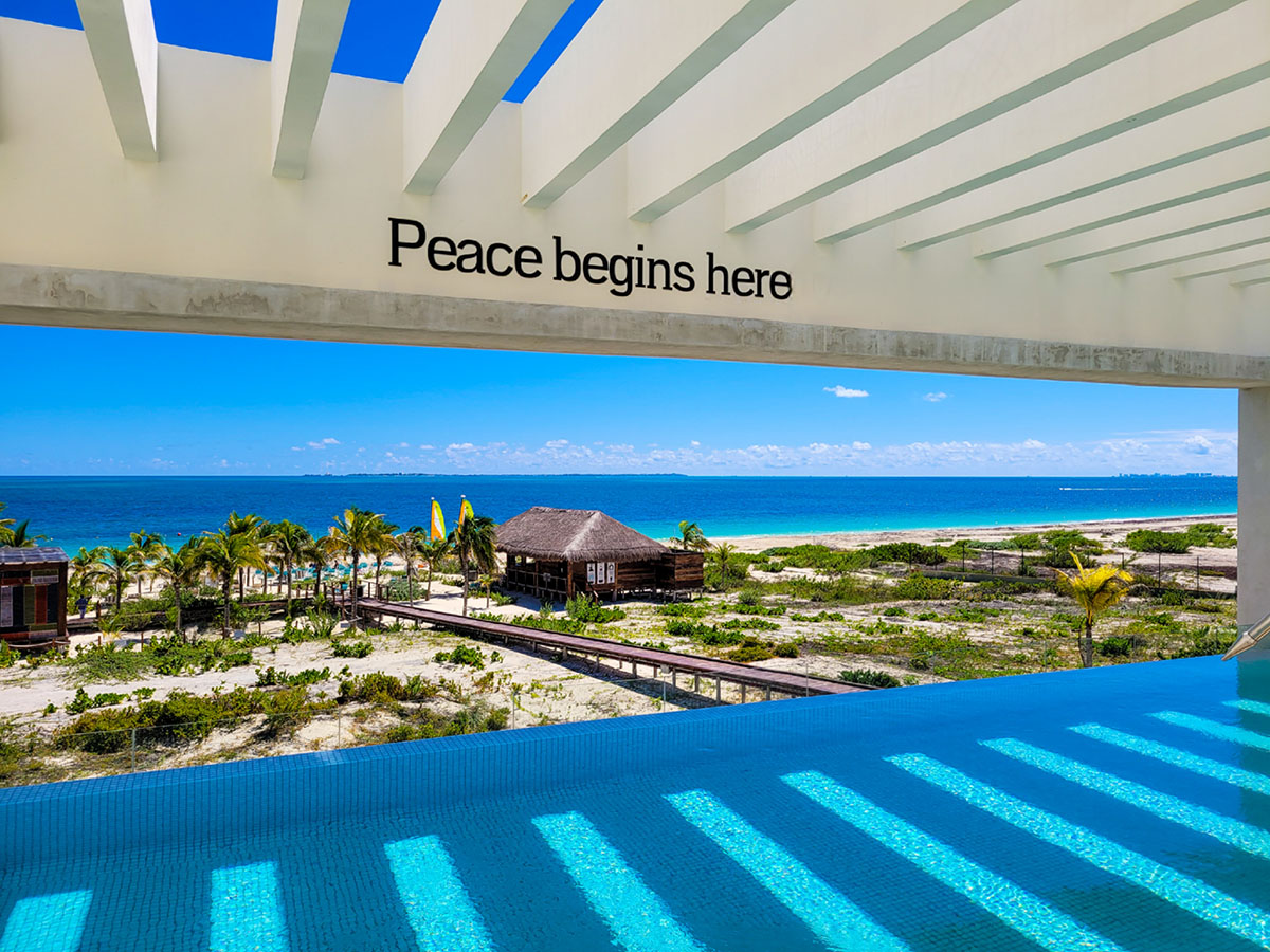 Looking out at the beach and ocean from an infinity pool in Cancun with a side reading "Peace begins here".