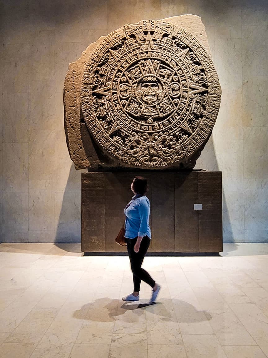 Ashlea walks in front of the Aztec Sun Stone looking up at the massive rock inside the Museum of Anthropology in Mexico City.