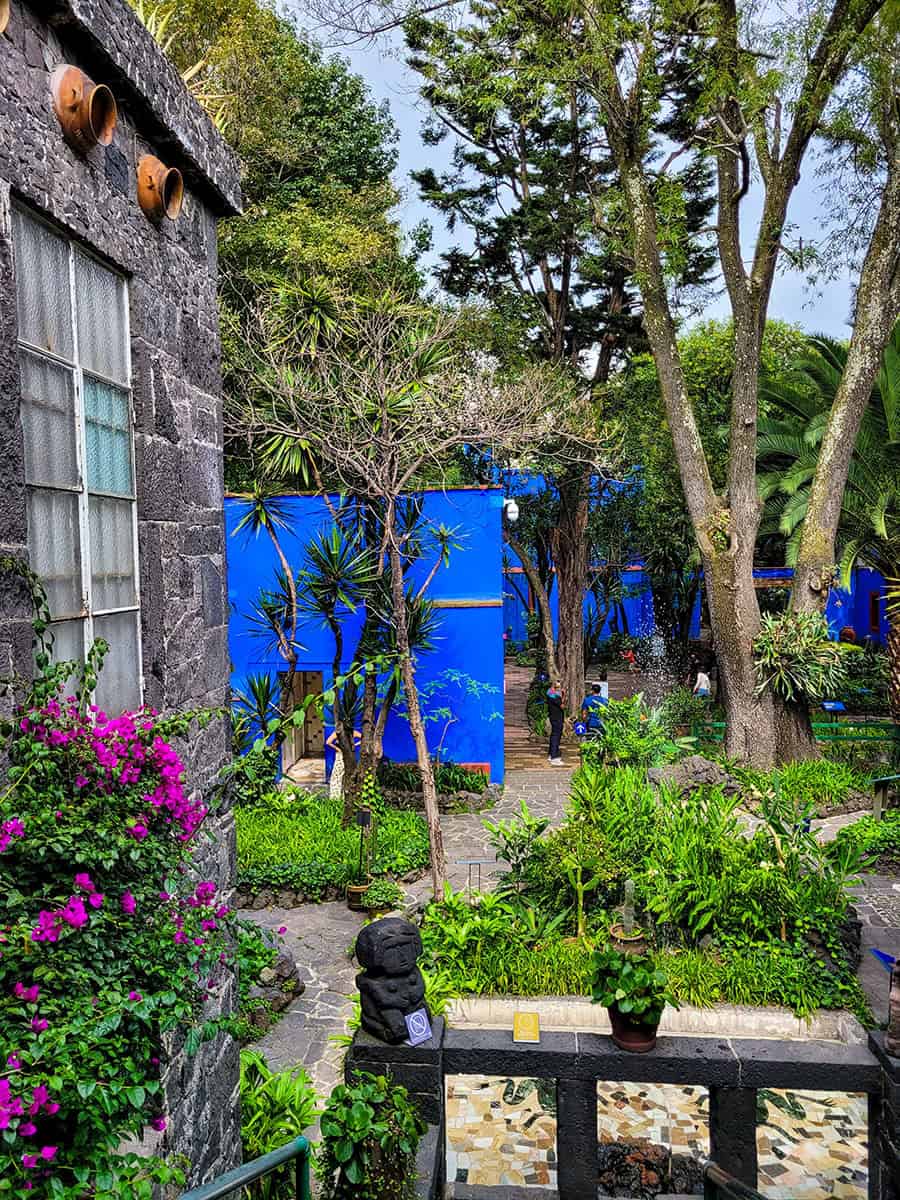 Looking out the window of Frida Kahlo's bedroom at the courtyard garden filled with trees, flowers, and bright blue walls.