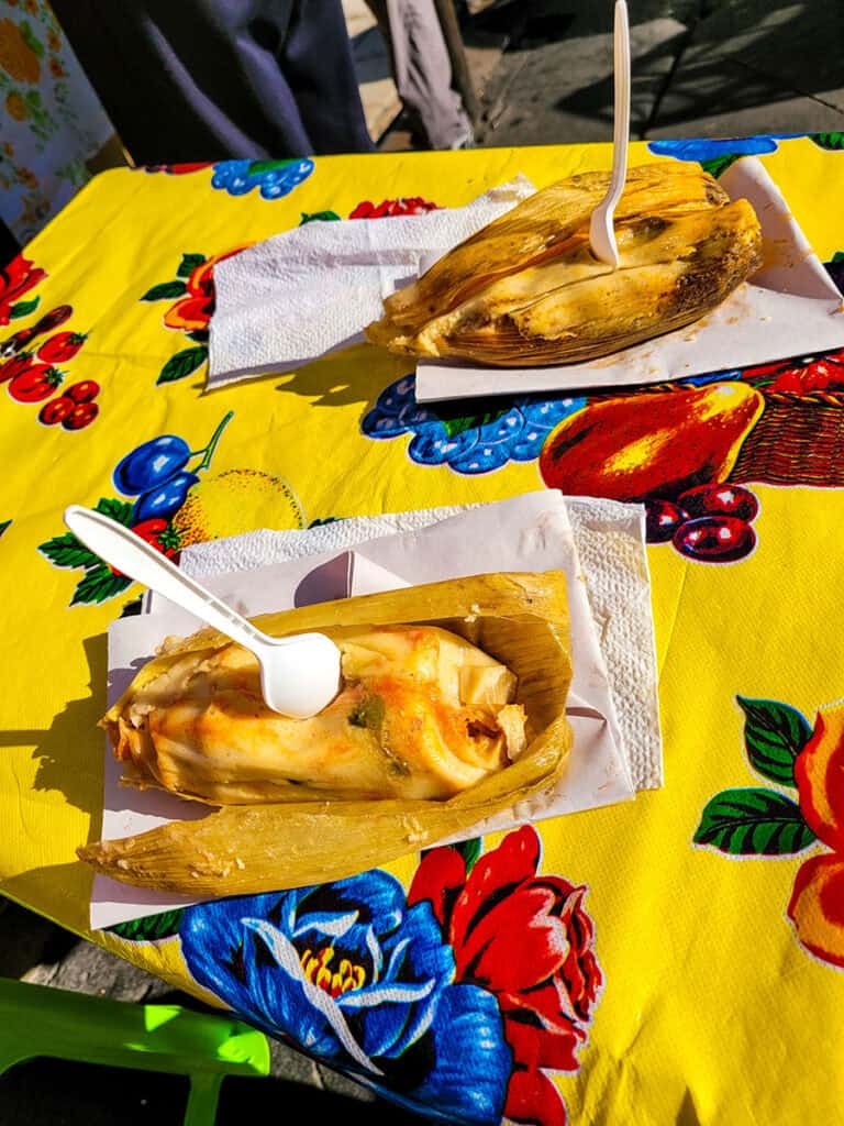 Two tamales with spoons sitting on a bright yellow tablecloth at a street food stand in Mexico City